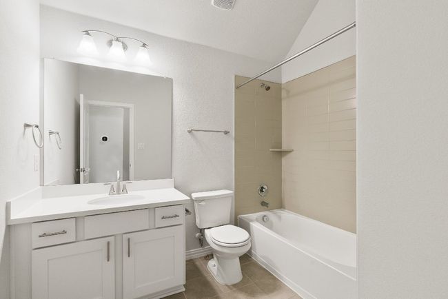 Full bathroom with vanity, shower / washtub combination, tile patterned flooring, vaulted ceiling, and a textured wall | Image 12