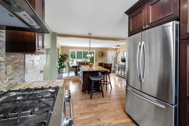 Kitchen with wall chimney range hood, light hardwood / wood-style floors, gas range, stainless steel fridge, and pendant lighting | Image 7