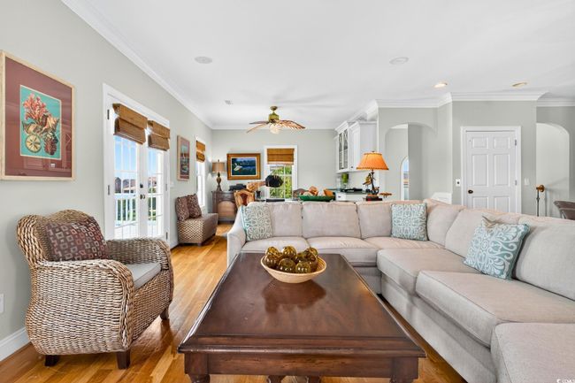 Living area with arched walkways, light wood finished floors, ceiling fan, crown molding, and recessed lighting | Image 6