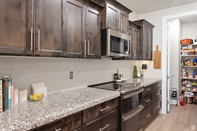 Kitchen featuring stainless steel appliances, dark brown cabinets, light stone counters, and light wood finished floors | Image 45
