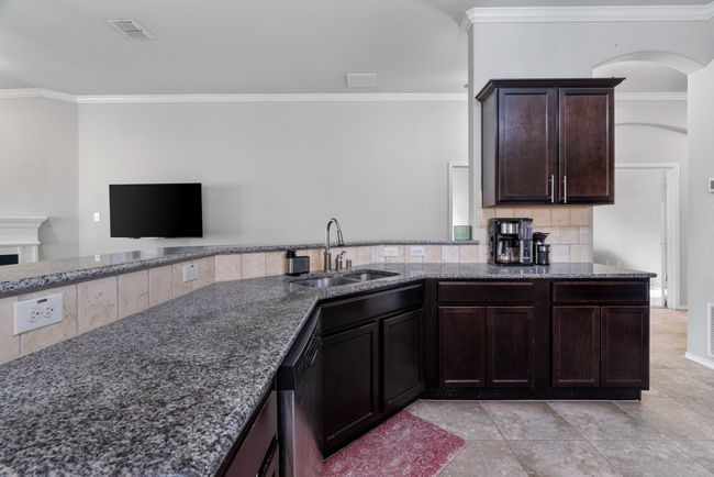 Kitchen with a sink, dark stone countertops, ornamental molding, dark brown cabinetry, and backsplash | Image 8