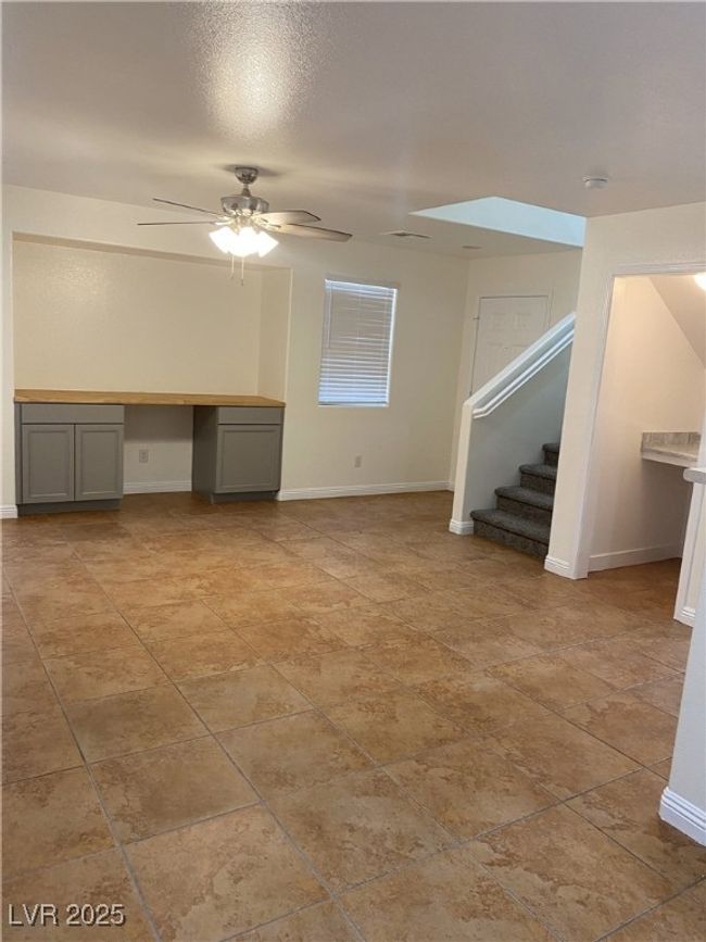 Unfurnished living room with built in desk, stairs, a ceiling fan, and baseboards | Image 19