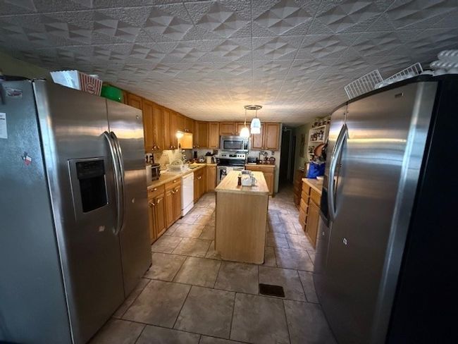Kitchen with hanging light fixtures, wood counters, appliances with stainless steel finishes, and a center island. One fridge to convey | Image 23