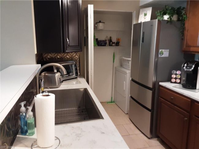 Kitchen with washing machine and clothes dryer, a sink, light tile patterned flooring, light countertops, and freestanding refrigerator | Image 9