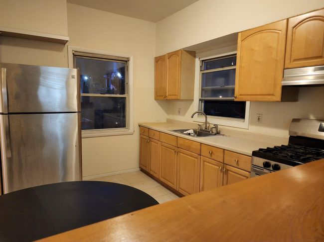 Kitchen with appliances with stainless steel finishes, under cabinet range hood, a sink, light tile patterned floors, and light countertops | Image 11