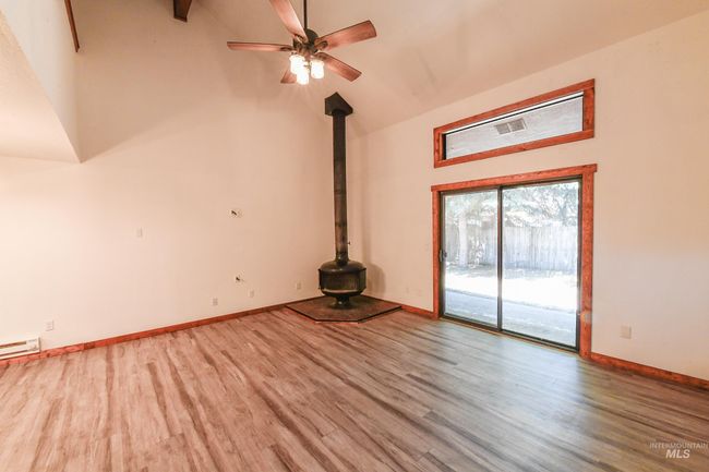 Unfurnished living room featuring a wood stove, wood finished floors, high vaulted ceiling, ceiling fan, and a baseboard radiator | Image 9