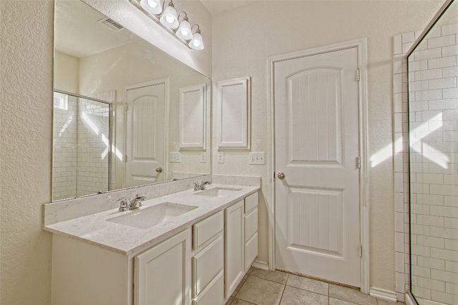 Bathroom with double vanity, tile patterned floors, a textured wall, and a tile shower | Image 21