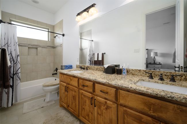Bathroom with a sink, shower / bathtub combination with curtain, double vanity, and toilet | Image 24
