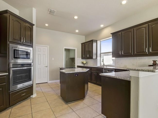 Kitchen with stainless steel appliances, dark brown cabinets, backsplash, a kitchen island, and recessed lighting | Image 7