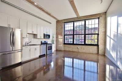 Kitchen featuring beam ceiling, brick wall, sink, appliances with stainless steel finishes, and white cabinetry | Image 1