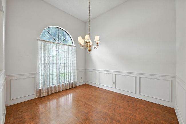 Spare room featuring a chandelier, a decorative wall, a wainscoted wall, lofted ceiling, and wood finished floors | Image 5