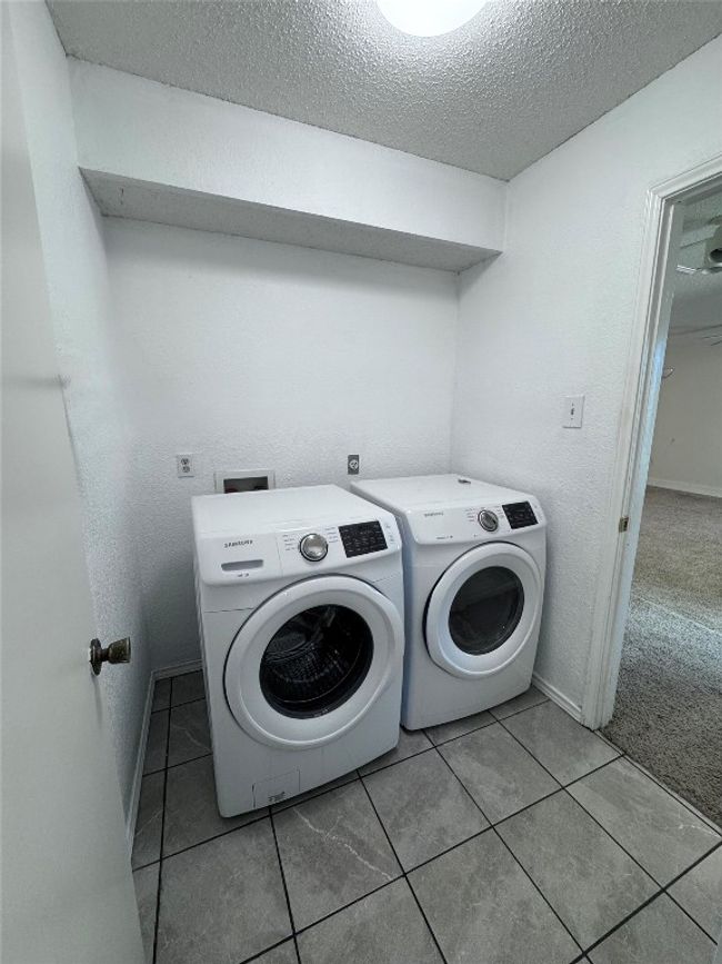Washroom featuring a textured ceiling, light tile patterned floors, separate washer and dryer, and a textured wall | Image 25