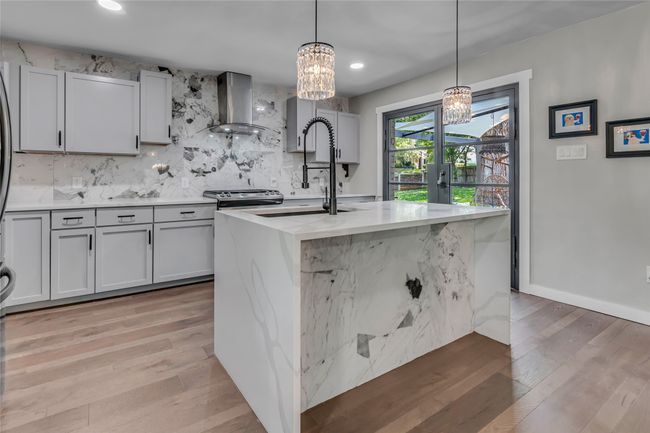 Kitchen featuring island range hood, a chandelier, backsplash, light wood finished floors, and hanging light fixtures | Image 11
