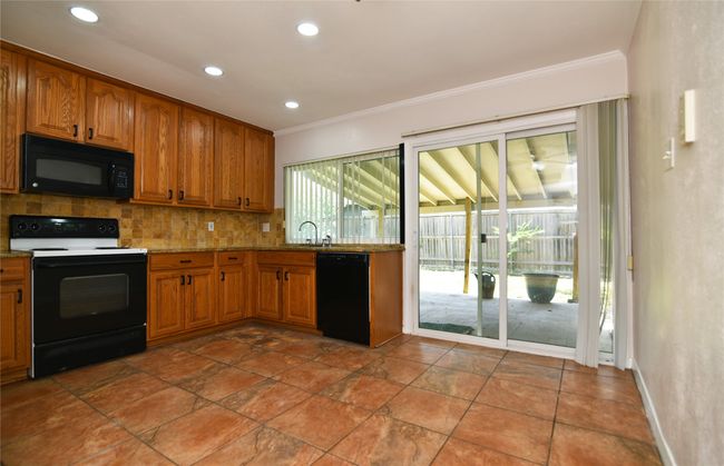 Kitchen with black appliances, ornamental molding, tasteful backsplash, brown cabinetry, and light stone counters | Image 9