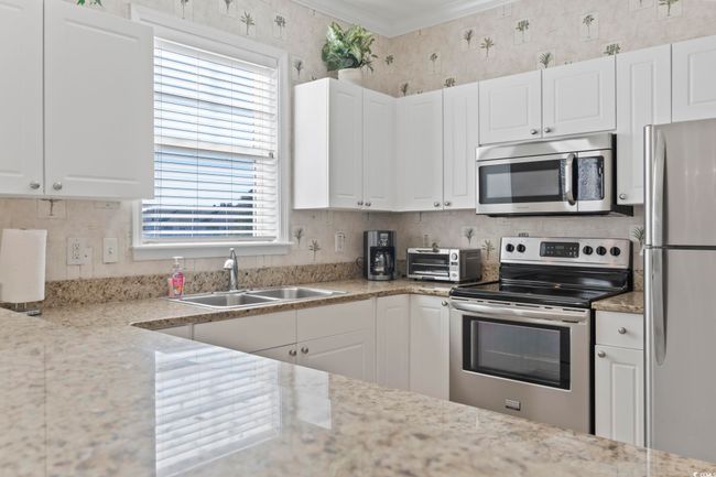 Kitchen with stainless steel appliances, a sink, white cabinets, wallpapered walls, and ornamental molding | Image 4