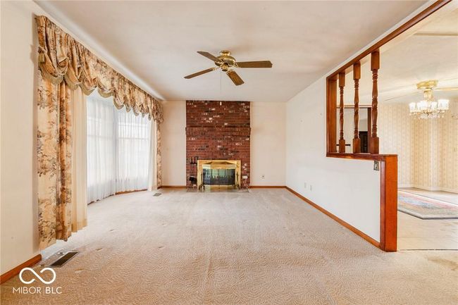 unfurnished living room featuring ceiling fan, a chandelier, carpet floors, a fireplace, and wallpapered walls | Image 20