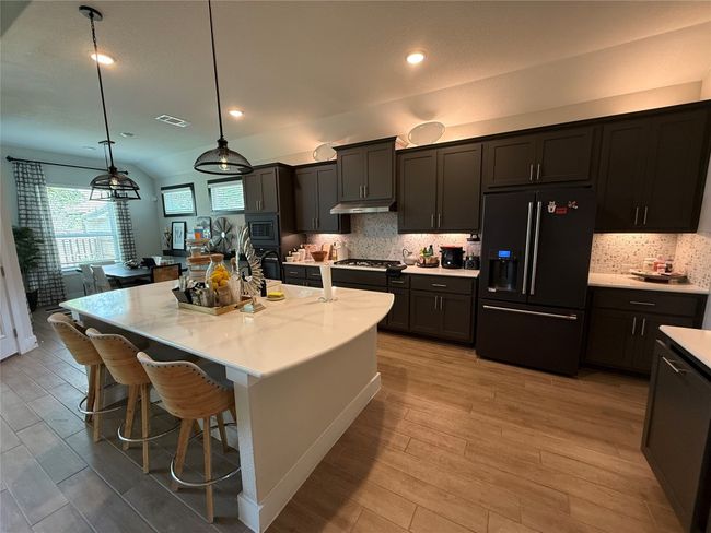 Kitchen featuring black appliances, under cabinet range hood, light wood-style floors, a breakfast bar, and recessed lighting | Image 9