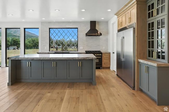 Kitchen with high end appliances, wall chimney range hood, a kitchen island, light wood-style floors, and backsplash | Image 19