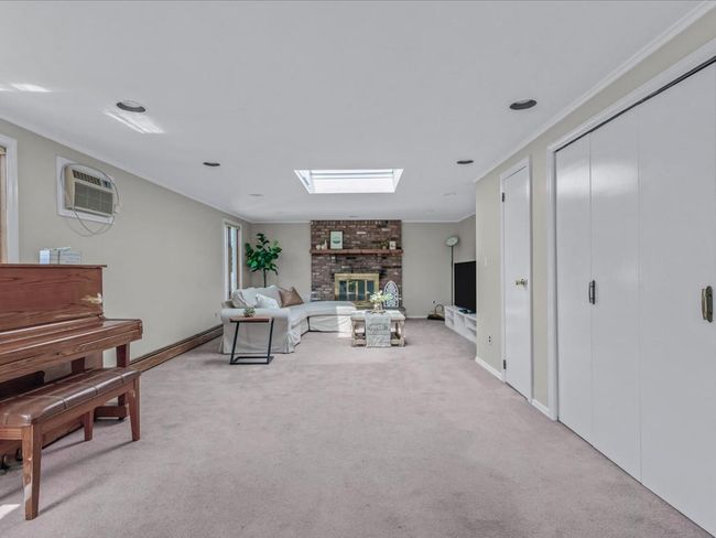 Living room featuring a brick fireplace, crown molding, a skylight, a wall unit AC, and light colored carpet | Image 12