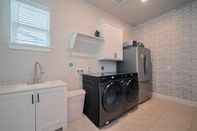 A large laundry room has a utility sink with storage, room for a fridge and/or deep freeze and a stylish brick-patterned accent wall. | Image 20