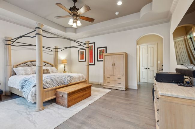 Bedroom with light wood-style flooring, a tray ceiling, arched walkways, baseboards, and ornamental molding | Image 10
