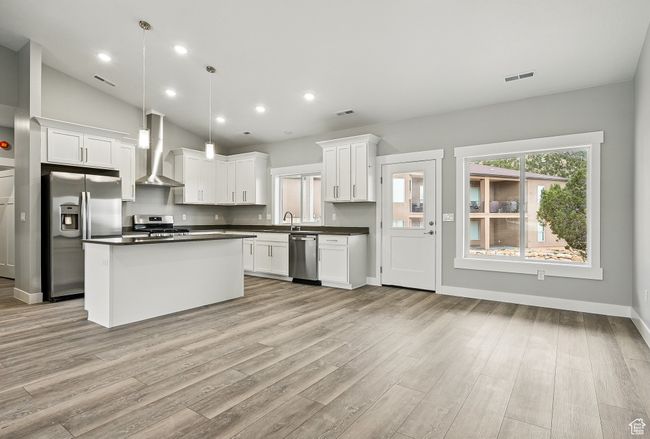 Kitchen with appliances with stainless steel finishes, wall chimney range hood, dark countertops, light wood-style floors, and white cabinets | Image 13
