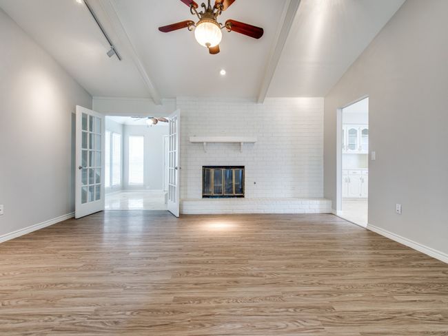 Unfurnished living room with ceiling fan, beamed ceiling, light wood-type flooring, a brick fireplace, and baseboards | Image 5
