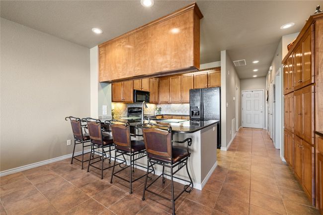 Kitchen featuring decorative backsplash, dark countertops, a breakfast bar area, a peninsula, and black appliances | Image 7