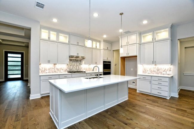 Kitchen featuring quartz countertops, white cabinetry, a sink, and under cabinet range hood | Image 11