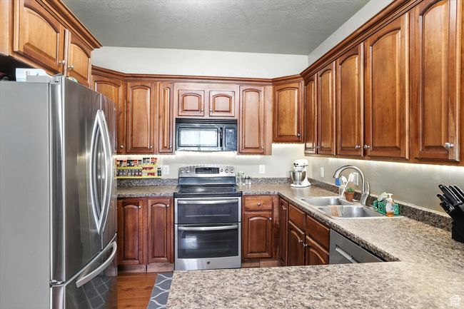 Kitchen with stainless steel appliances, dark wood-style flooring, brown cabinets, and a textured ceiling | Image 9