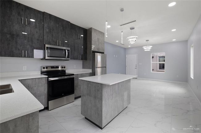 Kitchen featuring stainless steel appliances, modern cabinets, light marble finish floors, a center island, and recessed lighting | Image 4