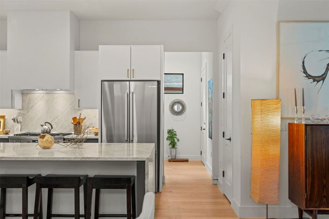 Kitchen featuring freestanding refrigerator, white cabinets, tasteful backsplash, light stone countertops, and light wood-type flooring | Image 19
