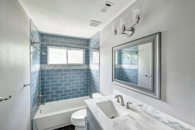 The updated full bath has a marble countertop and sleek tile. | Image 13