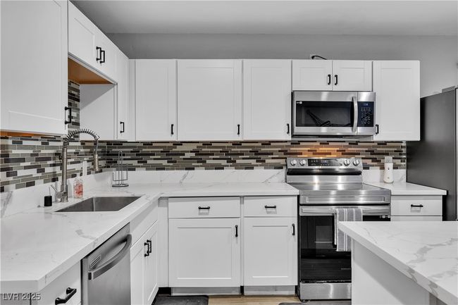 Kitchen featuring light stone countertops, a sink, stainless steel appliances, decorative backsplash, and white cabinets | Image 14