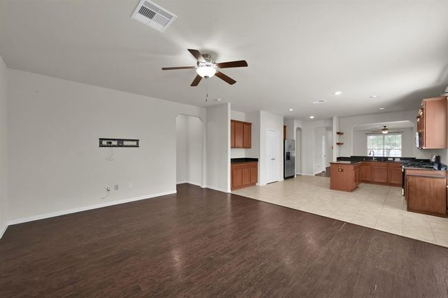 This spacious, open-plan living area features hardwood floors, a ceiling fan, and natural light from large windows. It seamlessly connects to a modern kitchen with stainless steel appliances and tile flooring, offering a perfect blend of comfort and functionality. | Image 15