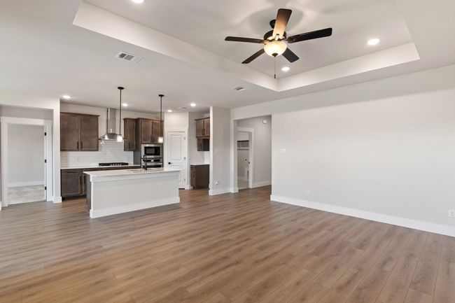 Kitchen featuring wall chimney exhaust hood, stainless steel appliances, a raised ceiling, open floor plan, and ceiling fan | Image 8