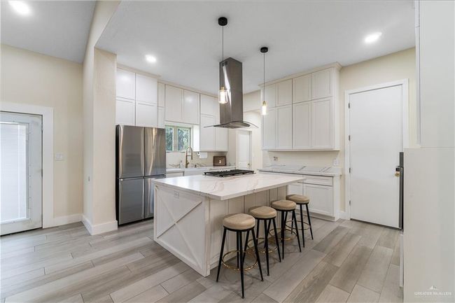 Kitchen with light hardwood / wood-style flooring, decorative light fixtures, stainless steel appliances, island range hood, and a center island | Image 22