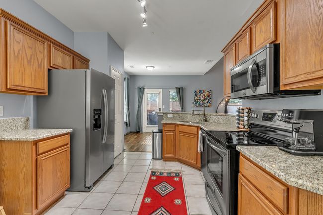 Kitchen featuring stainless steel appliances, a peninsula, light tile patterned flooring, brown cabinetry, and light stone countertops | Image 8