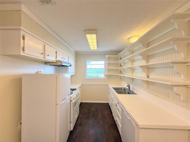 Kitchen with white appliances, under cabinet range hood, dark wood finished floors, white cabinets, and open shelves | Image 7