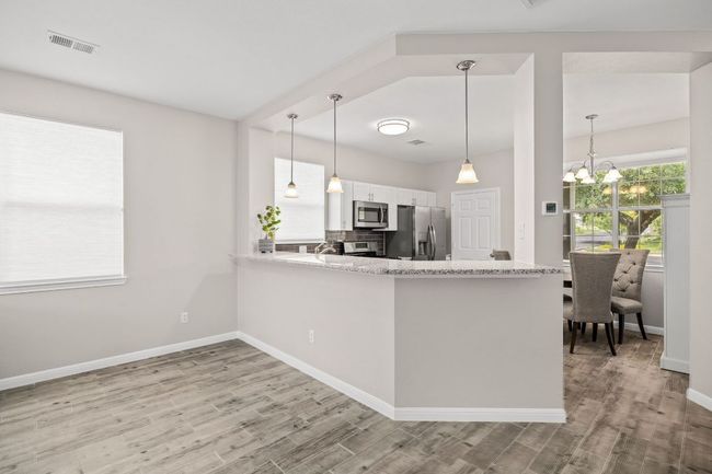 Kitchen with white cabinetry, visible vents, stainless steel appliances, baseboards, and wood finished floors | Image 14