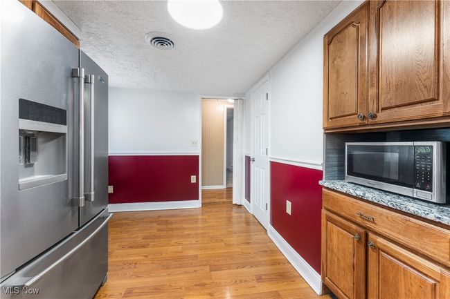 Kitchen with a textured ceiling, appliances with stainless steel finishes, light wood-style floors, visible vents, and baseboards | Image 13