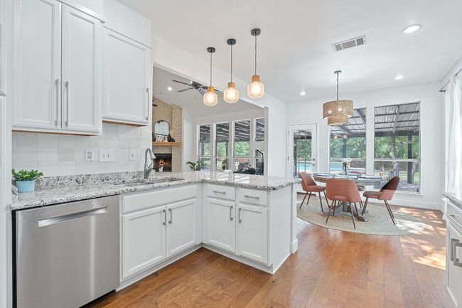 Kitchen with a ceiling fan, dishwasher, a peninsula, a brick fireplace, and white cabinetry | Image 10