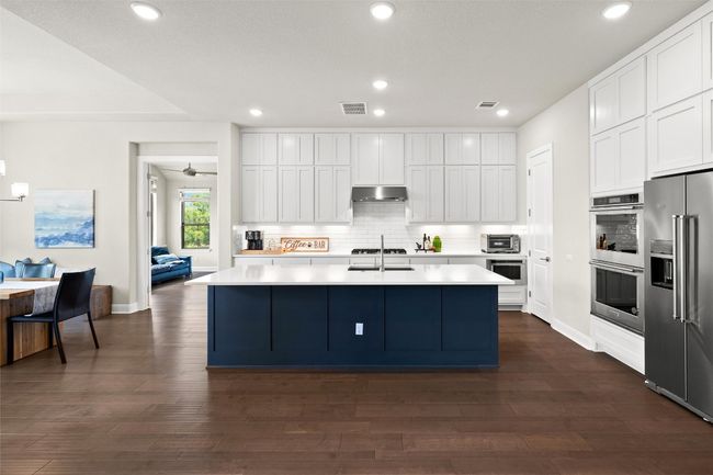 Kitchen featuring appliances with stainless steel finishes, under cabinet range hood, decorative backsplash, a center island with sink, and white cabinets | Image 16