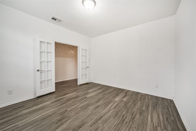 The study features clean white walls and wood flooring, with double French doors connecting to an adjacent space. The ceiling light provides ample illumination, and the overall design offers a versatile area for various uses. | Image 7