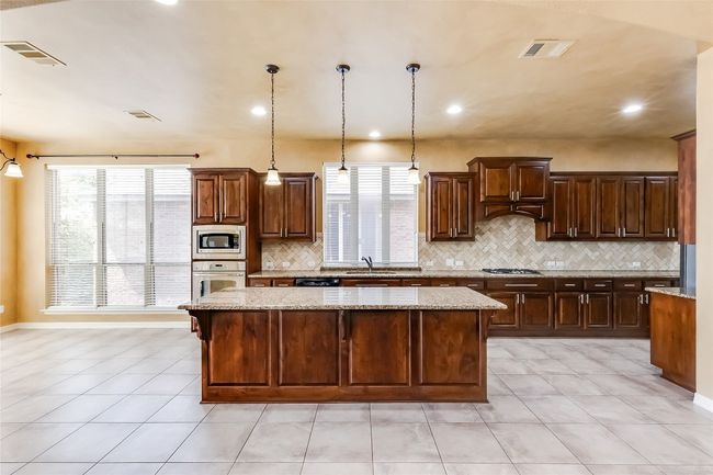 Kitchen featuring decorative backsplash, visible vents, a kitchen island, appliances with stainless steel finishes, and a sink | Image 12