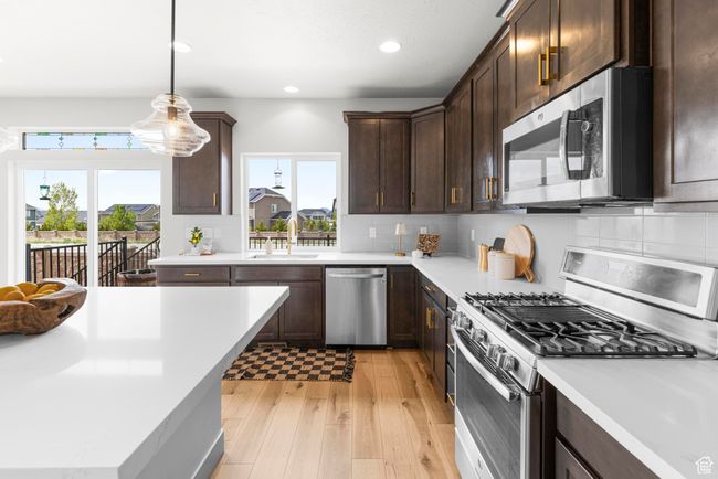 Kitchen featuring a sink, appliances with stainless steel finishes, light wood-style floors, light countertops, and dark brown cabinetry | Image 12