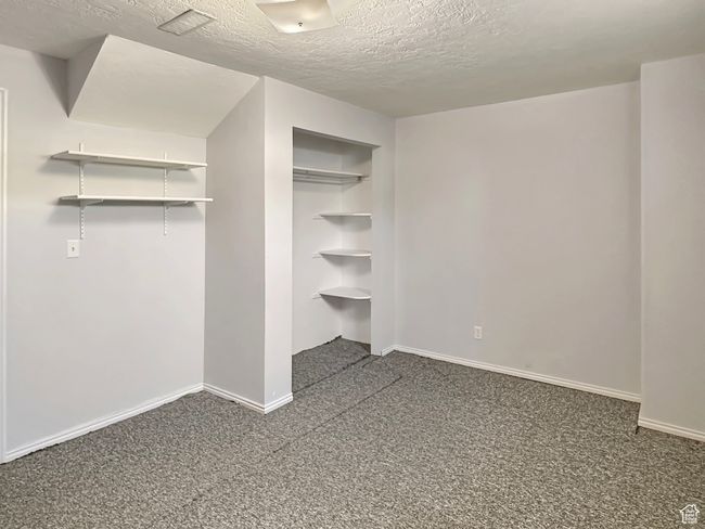 Unfurnished bedroom with a textured ceiling, dark colored carpet, baseboards, and a closet | Image 26