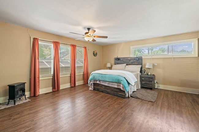 Bedroom featuring wood finished floors, baseboards, a wood stove, and ceiling fan | Image 9