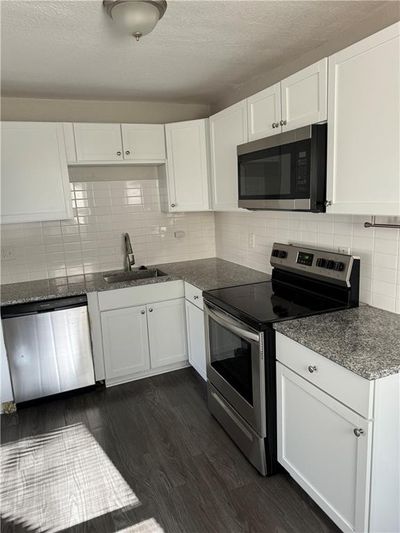 Kitchen with dark wood-type flooring, white cabinetry, sink, and stainless steel appliances | Image 3