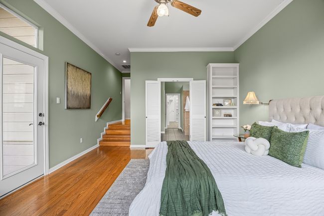Just three steps down from the main level, the primary bedroom offers privacy and charm with original hardwood floors, a wall of windows overlooking the trees, and direct access to the screened porch. Stationary louvered doors lead to the ensuite bath. | Image 24
